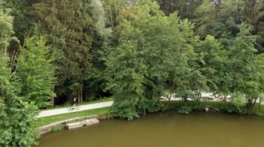 Bir sporcu gölün etrafında gerçekten hızlı bisiklet sürüyor. Başka bir motosikletçi ters yöne gidiyor..