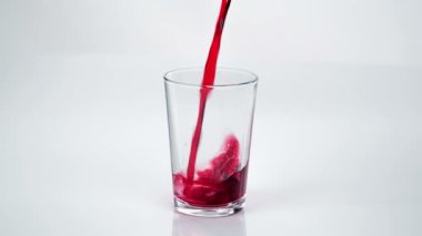 Birisi mutfak tezgahındaki boş bardağa kırmızı meyve suyu döküyor..