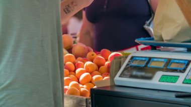 Genç bir manav müşterisi için kahverengi bir kesekağıdına biraz daha taze kayısı koyuyor ve karşılığında para alıyor..