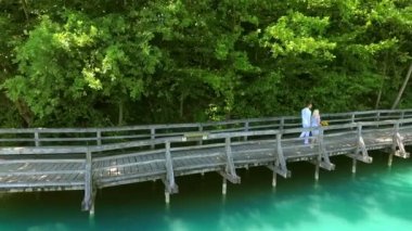 Bir kadın elinde erkek arkadaşının onun için getirdiği çiçekleri tutuyor. Gölün etrafında bir patikada yürüyorlar. Hava görüntüsü.