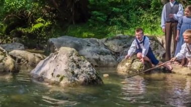 Eski moda kıyafetler giymiş çocuklar su kenarında oturuyorlar ve takılıyorlar. Güzel, güneşli bir gün..