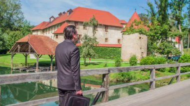 Köprünün bir tarafında muhteşem bir kale duruyor. Siyah takım elbiseli bir iş adamı köprüden geçer. Hava güneşli ve doğa çok güzel..