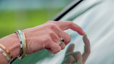 Genç bir kadın arabanın camına dokunuyor ve yeterince temiz mi diye kontrol ediyor..