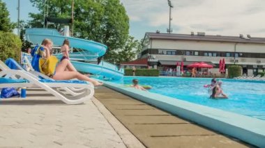 DOMZALE, SLOVENIA - 20. Haziran 2015 'te kızlardan biri iskemlede uzanıyor ve güneşleniyor. Arkadaşlarının geri kalanı havuzda yüzüyor. Güzel ve güneşli bir yaz günü..