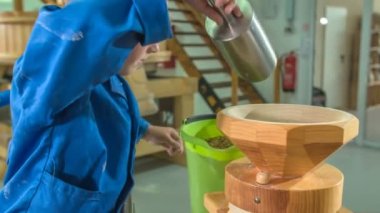 Bir öğrenci tohumları küçük bir ahşap değirmene yerleştiriyor ve sonra öğütüyor..