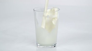 Birisi mutfaktaki masada duran boş bir bardağa taze süt döküyor..