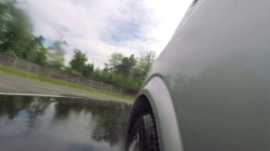 Bir araba ıslak bir yolda sürer ve bir dönüş yapar. Bu güvenli bir sürüş merkezinde gerçekleşiyor. Yakın çekim..