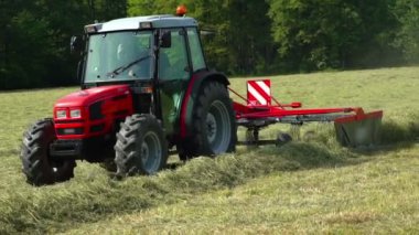 Bir çiftçi traktörünü sürüyor, saman hazırlıyor ve onu farklı hatlara ayırıyor. Böylece daha sonra bir karavana koymak onun için daha kolay olur. Sıcak bir yaz günü..