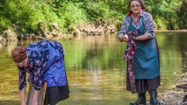 Çok yaşlı kadınlar güneşli bir günde nehirde çamaşır yıkıyorlar. Ayrıca çok geleneksel kıyafetler giyiyorlar..