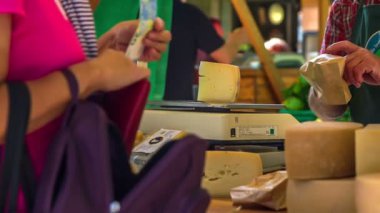Bir bayan pazardan peynir satın alıyor. Bir adam onu dikkatlice kahverengi bir kesekağıdına koyar..
