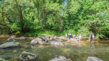 Genç bir çocuk bir kayanın tepesinde duruyor, uzaktan birini görüyor ve ona el sallıyor. Çocuklar nehir kenarında takılıyor..