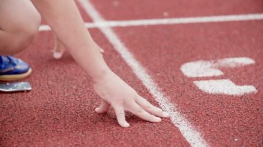 Eller sınırdan önce gelir. Bir çocuk koşmaya başlamak üzere. Okulun dışındaki koşu pistinde beden eğitimi dersi veriyor..