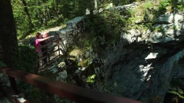 İki yürüyüşçü çitin yanında duruyor ve bir şeyi işaret ediyorlar. Çitin diğer tarafında tehlikeli bir delik var..