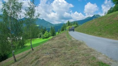 Traktörlü genç bir çiftçi beton yolda gidiyor ve çimen tarlasına yaklaşıyor..