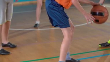 Öğrenciler bir okul spor salonunda basketbol oynuyorlar. Okul terliği giyiyorlar..