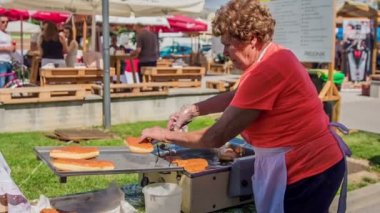 DOMZALE, SLOVENIA - 15. HAZİRAN 2018 Yaşlı bir kadın kızarmış donut yapıyor ve pişince çok sıcak oldukları için onları çabucak çıkarıp tabağa koyuyor..