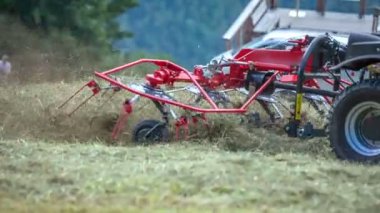 Genç bir adam traktörünü kullanıyor ve tarımsal makinelerle samanların etrafında dolanıyor..