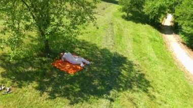 Genç bir çift birlikte eğleniyor. Ağacın altında öpüşüyorlar. Çimleri biçilmiş bir gölün yanında..