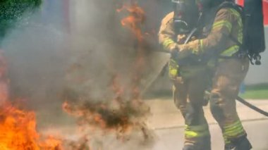 DOMZALE, SLOVENIA - 7. Temmuz 2018 'de iki itfaiyeci bir tüpü bir arada tutuyor ve yangını söndürüyorlar. Yangın çok yayıldı ve büyük siyah bir duman da görebiliyoruz..