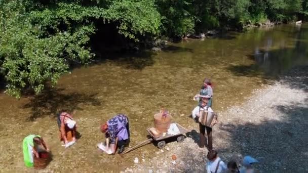 Mosónő Ruhákat Mos Folyóban Gyerekek Játszanak Táncolnak Valaki Harmonikázik — Stock videók