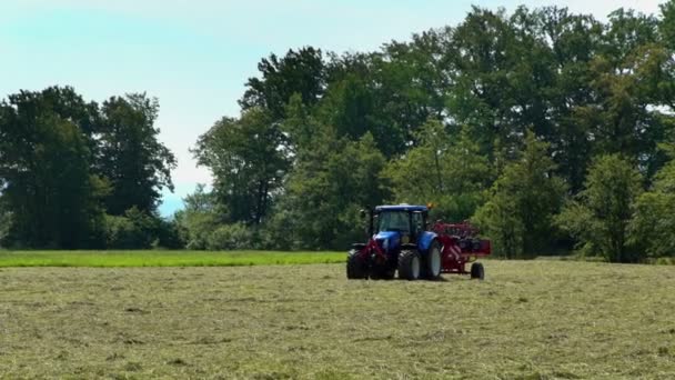 Een Grote Blauwe Trekker Trekt Een Draaiende Hark Machine Achter — Stockvideo