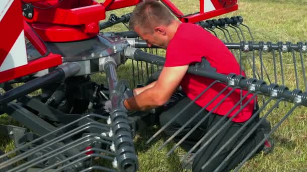 若い男がひざまずいて 彼は農業機械の下部に何かを修正しています 安全作業用の手袋をしてる — ストック動画