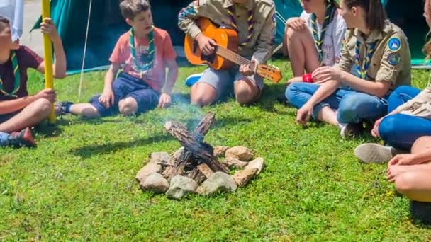 若い斥候のグループが歌を歌い 最も古い斥候の1つはテントの前で火を点けている ロイヤリティフリーのストック動画