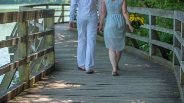 若いカップルは恋にあり 彼らはデート中です 彼らは湖を歩いている彼女は手にひまわりの花束を持っている — ストック動画