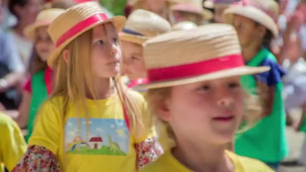 小さな子供たちが黄色と緑のシャツとわらの帽子をかぶっていて お互いに手をつないで群衆の間を歩いています — ストック動画