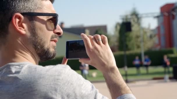 Domzale Slovenia 2018年6月一个年轻人拿着他的手机 他在录一些东西 今天是夏天 他戴着太阳镜 — 图库视频影像
