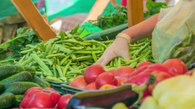 Bir manav eldiven takıyor ve müşteri için bir torbaya bir sürü yeşil fasulye koyuyor..
