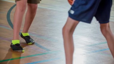 Çocuklar basketbol potasına atmadan önce topu sektiriyorlar. Okulun spor salonunda spor yapıyorlar..