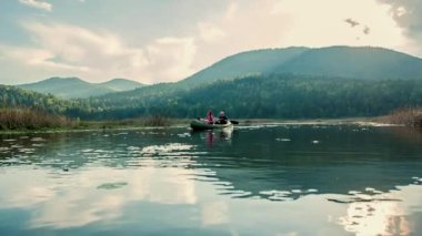 Bir çift kanoda kürek çekiyor. Su huzur dolu. Arka planda bir dağ daha var..