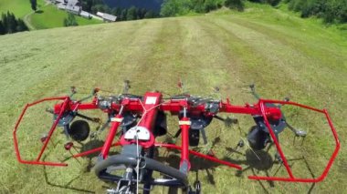 Bir traktör kesilmiş çimlerle büyük bir alanda sürüyor ve arkasında tarım makinelerini çekiyor..