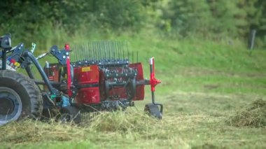 Traktör sürerken döner tırmıklar çok hızlı hareket eder. Genç bir çiftçi çiftlikteki hayvanlar için saman hazırlıyor..