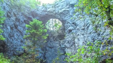 İki kişi bastonlarıyla yürüyüş yapıyor. Şu anda, bir yolun ortasında durdular ve bir kayanın ortasındaki deliğe bakıyorlar..