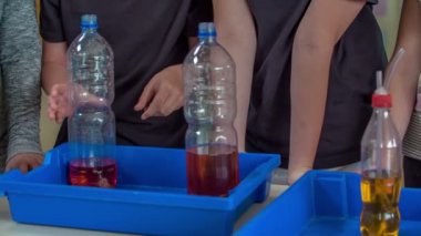 Öğrenciler kimya dersinde bir deney yapmaya hazırlar. Plastik şişeleri ve özel kırmızı sıvıları var..
