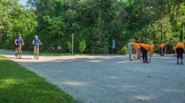 DOMZALE, SLOVENIA - 21. Haziran 2015 'te bir grup son sınıf öğrencisi spor yapıyor ve bisikletli iki kişi geçiyor. Güzel bir yaz günü..