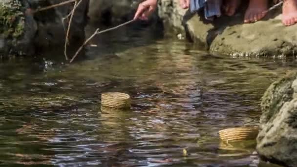 孩子们站在河岸上 试着用树枝到河边的小木篮上 — 图库视频影像