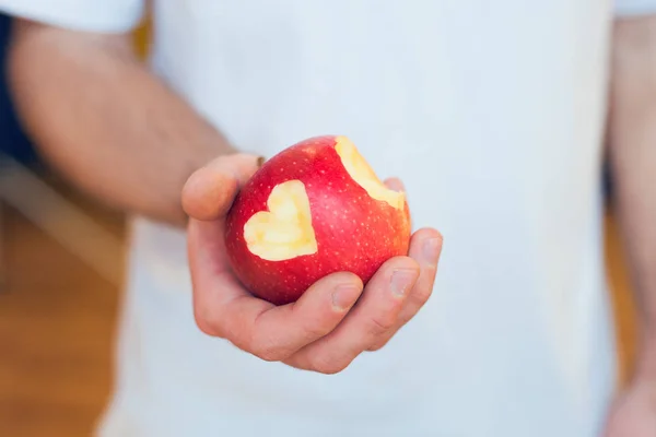 Bitten red apple with cutted heart in the male hand