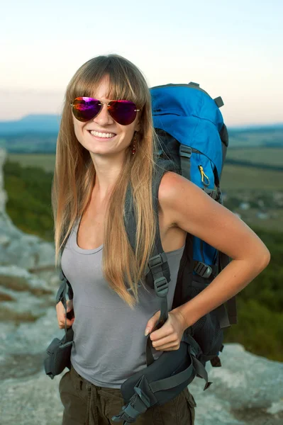 Mulher nova de sorriso com a trouxa nas montanhas — Fotografia de Stock