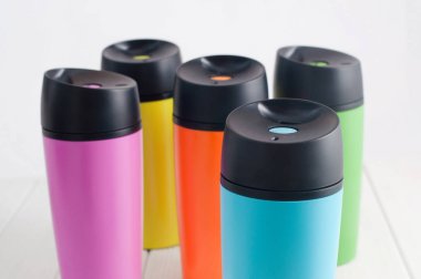 Beyaz ahşap masada renkli termos bardakları