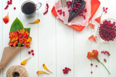 Bir fincan kahve, kek ve çiçekler beyaz ahşap arka planda.