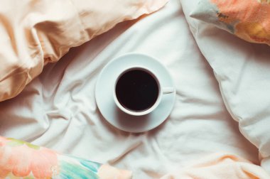 Beyaz çarşaflı bir yatakta bir fincan kahve.