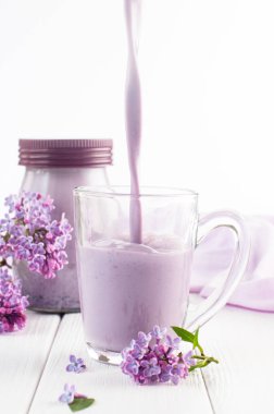 Leylak çiçeklerinin yanında yabanmersinli milkshake dolu cam bardak.