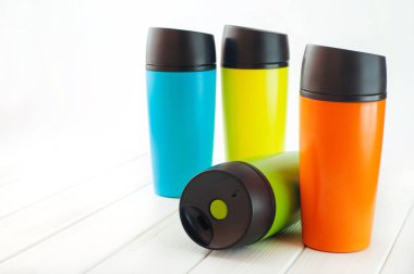 Beyaz arka plandaki beyaz ahşap masada renkli termos bardakları