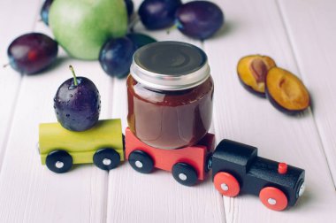 Bebek mamasıyla kavanoz, erik püresi ve oyuncak tahtanın üzerinde taze erik.