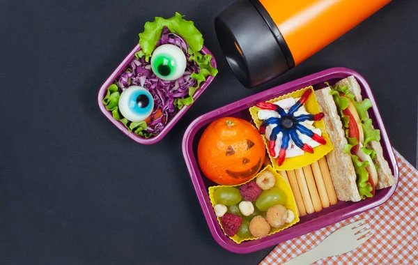 Open Halloween lunch box with school lunch near thermo mug on bl — Stock Photo, Image