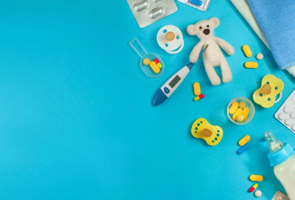 Таблетки и медвежья игрушка с электронным термометром на синем фоне — стоковое фото
