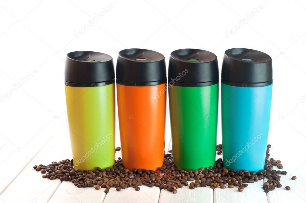 Four thermos mugs near coffee beans on the white background